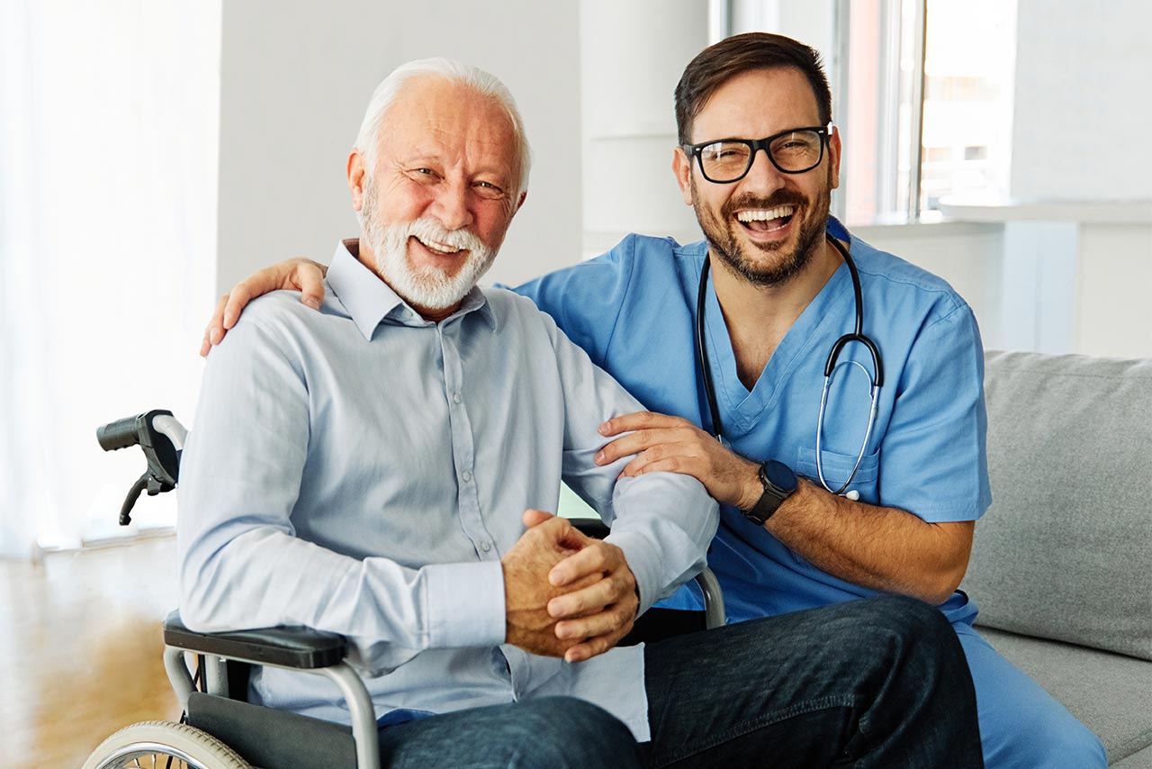 An elderly man in a wheelchair with a smiling nurse.