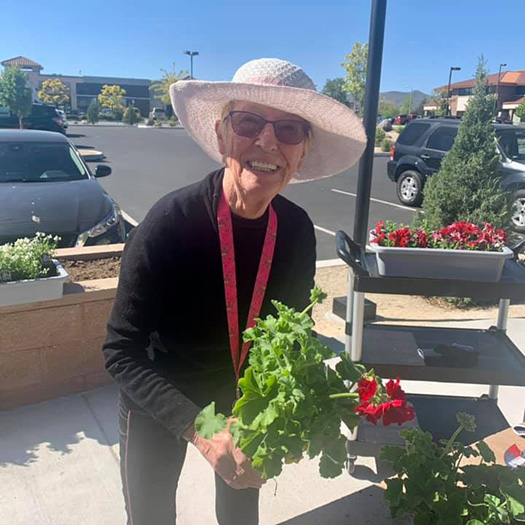 A woman in a hat holding a plant in front of a store.