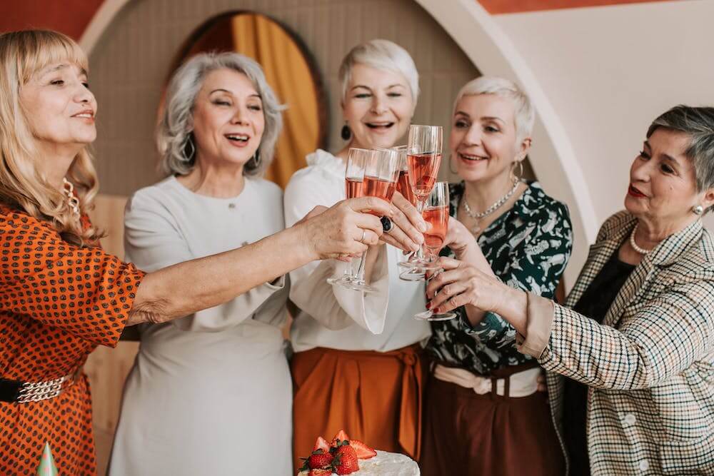 A photo of a group of senior women toasting to a birthday cake.