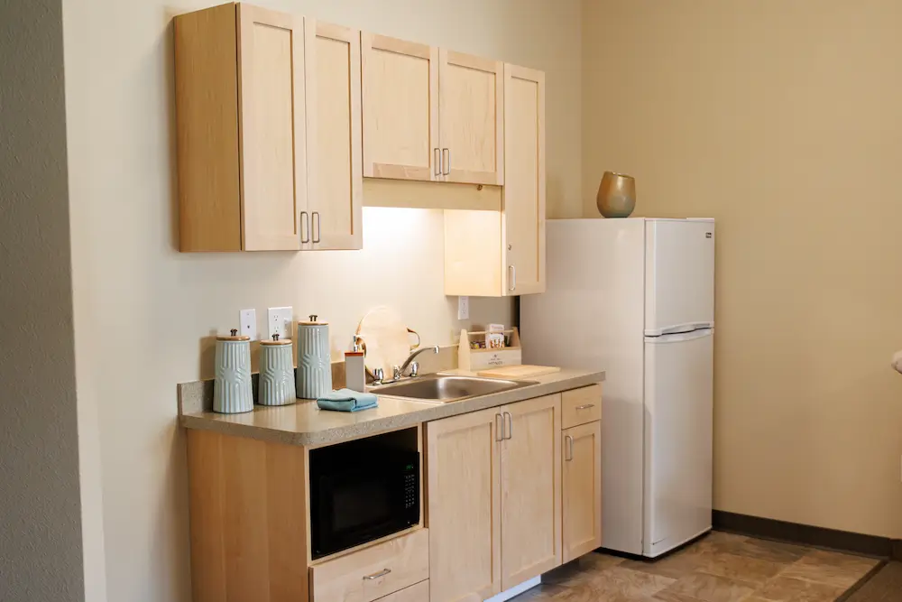 Compact kitchen with light wood cabinets, a white refrigerator, and a counter holding a microwave and small appliances.