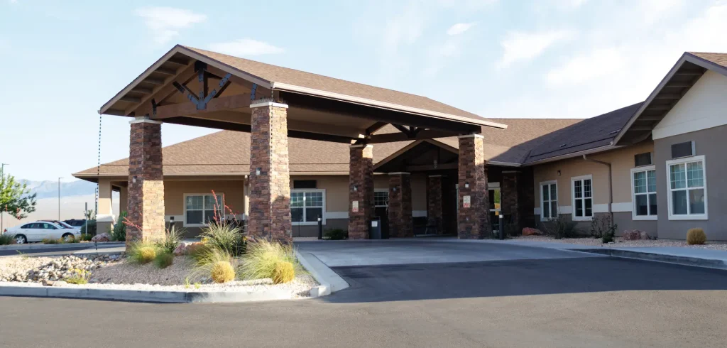 A single-story building with a stone-clad entrance canopy supported by columns, a paved driveway, and desert landscaping.